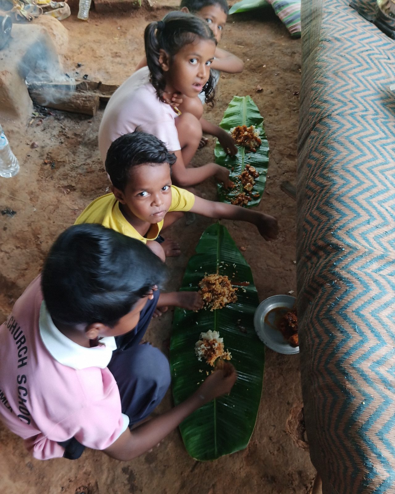 Children sharing a meal served on banana leaves in a rural setting, documented during fieldwork